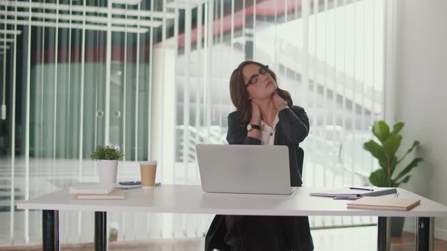 Healthy Workplace and Employee Wellbeing. Office Manager Performs Cervical Spine Stretch and Neck Relaxation at Desk to Prevent Pain, Support Mental Health, add Balance to Work and Corporate Wellness