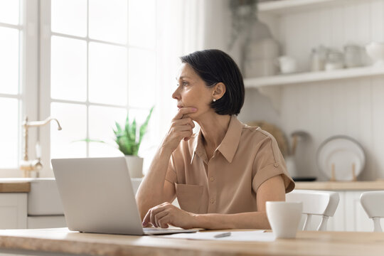Pensive mature female hesitating over business decision by notebook screen