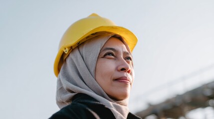Asian woman in hijab and hard hat gazes skyward, embodying Women in Construction Week, weaving hope and industry