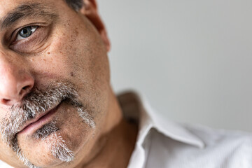 High-detail close-up image of the left side of a mature man's face, showcasing natural skin texture, blue eye, and a distinctive salt-and-pepper mustache.