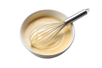 Close up overhead view of a metal whisk blending a creamy yellow batter or sauce in a white bowl against a black background