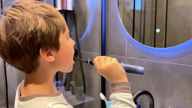 8 year old boy in modern bathroom brushing teeth with electric brush