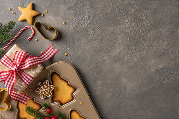 A festive Christmas and New Year baking scene shows a dark surface with a metal baking tray, star and tree cookies, candy cane, sprigs, a gift box with red gingham ribbon