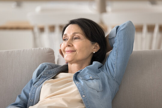 Tranquil smiling older woman relaxing on sofa hand behind head