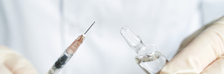 Close-up of gloved hands handling syringe and ampoule for medical procedure or vaccine administration.
