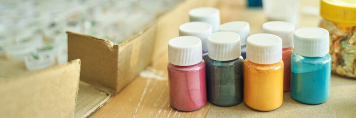 Vibrant assortment of acrylic paint jars with lids on wooden table for artistic creativity.