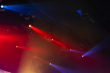 Energetic concert scene featuring red and blue spotlights cutting through haze