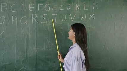 Video English basic online concept. Happy Asian woman teacher standing holding a pointer and teaching English language lesson on the blackboard via video call in the classroom. Back to school concept.