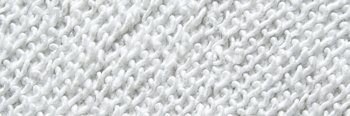 Close-up texture of white knitted fabric with intricate patterns and soft fibers visible.