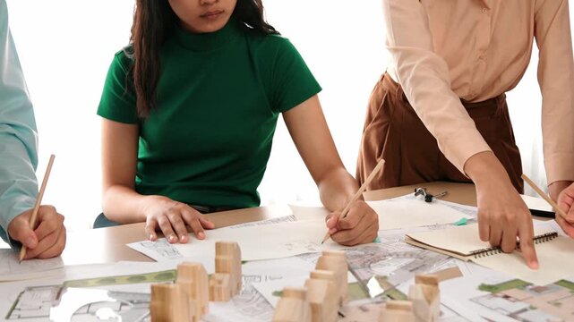 Smart architect and safety engineer discussion about building blueprint on table with architectural document, measurement tools and wooden block scatter around at modern office. Closeup. Delineation.