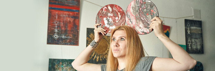 Young caucasian female holding two artistic discs with abstract designs in modern art gallery.