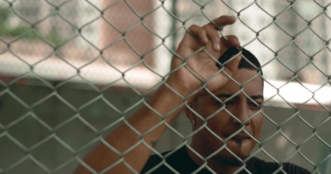 Latin Hispanic man of African descent gripping fence in anger and deep regret, expressing frustration, guilt, and emotional conflict in tense urban portrait