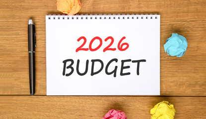 Fototapeta premium 2026 Budget symbol. Concept words 2026 Budget on beautiful white note. Beautiful wooden background. Black pen. Colored paper. Business and 2026 budget concept. Copy space.