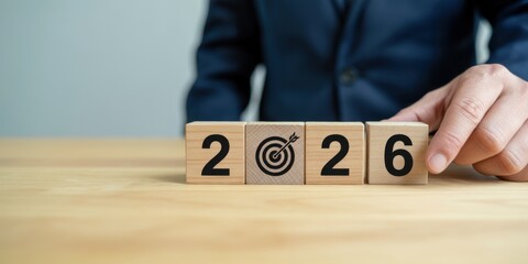Vision for 2026: A person's hand meticulously arranges wooden blocks to display the year 2026, the bullseye symbolizes future goals and objectives, evoking a sense of planning and anticipation.
