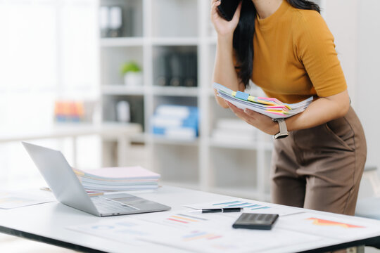 Workplace in Focus: A focused individual in a professional setting, engrossed in a discussion on a phone call while multi-tasking and assessing detailed documents at her desk.