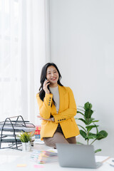 Confident Businesswoman on Phone: A radiant businesswoman, poised in her bright office, engages in a phone call, exuding confidence and professionalism, with her laptop and office supplies nearby.
