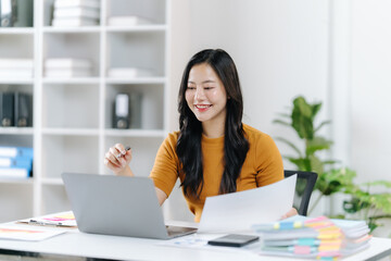 Focused Work: A woman, engrossed in her work, meticulously reviews documents and operates a laptop. The office environment exudes professionalism and efficiency.