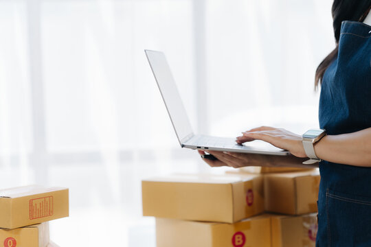 Digital Commerce and Order Processing: A professional utilizes a laptop to manage online orders amidst a collection of packages, representing efficiency in e-commerce and retail operations.