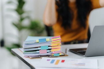 Document Focus: A stack of organized documents with colorful tabs rests on a desk in a workspace. A person, and a laptop are blurred in the background.