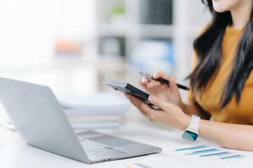 Focused Professional Calculation: A professional woman intensely concentrates on financial tasks, using a calculator alongside a laptop, with charts indicating financial progress.