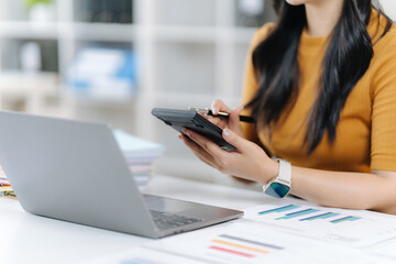Calculating Finances: A focused individual meticulously examines financial data at the workplace, with the laptop and calculator at the ready. A calm and composed atmosphere