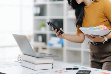 Work Productivity: a woman, engrossed in her workspace, focuses on a smartphone, document, and laptop, representing the intersection of efficiency, knowledge and business.