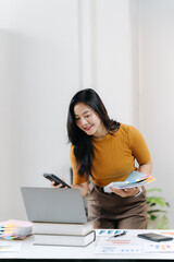 Efficiency in the Office: A professional woman focused in a modern workspace. She is holding swatch, and holding phone in a seamless blend of technology and design while looking towards laptop