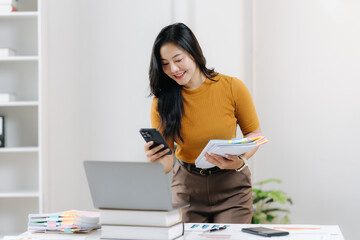 Digital Age Office Interaction: A focused woman in a warm-toned sweater actively engaging with her smartphone and documents, at a modern office desk setting, signifying connectivity and productivity.
