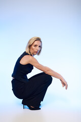 Elegant blonde woman poses in stylish black attire against a soft blue background
