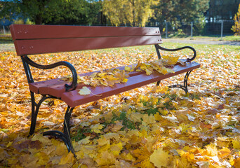 A park bench with a wooden seat and backrest, painted dark red, and black wrought-iron legs. A...