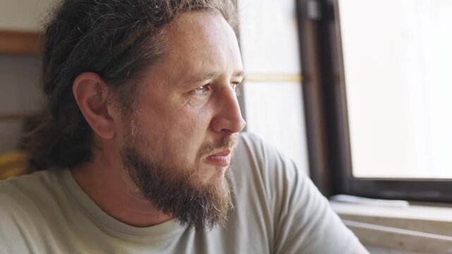 Thoughtful man with dreadlocks eating meal by the window