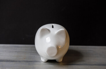A classic white piggy bank is placed on a rustic wooden table. Perfect for financial concepts and...