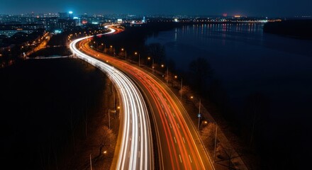 Fototapeta premium Long exposure night shot of a curved city road with bright car light trails by a river