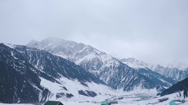 Snow covered mountains and village at Sonamarg, Jammu and Kashmir, India. Winter landscape. Dark clouds in sky and snowfall in high mountain peaks. Tourism and vacation background. Winter wonderland.