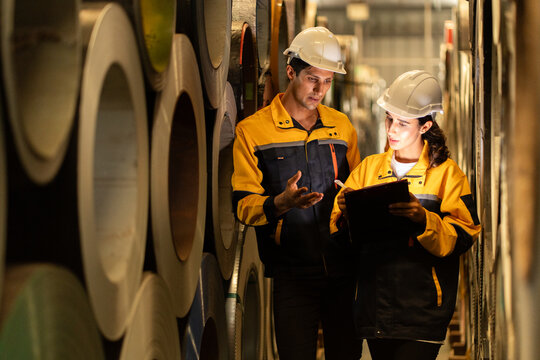 two Industrial engineers inspecting large metal rolls in warehouse storage. Wearing safety uniforms and helmets. inventory check, manufacturing logistics, and factory teamwork. engineer, two worker. - Powered by Adobe