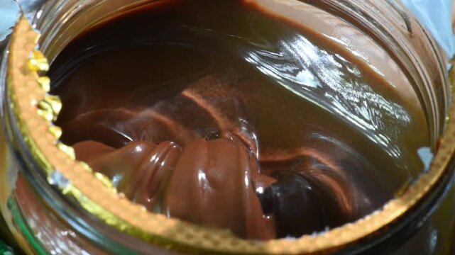Taking chocolate cream from a jar with a fork, close-up.