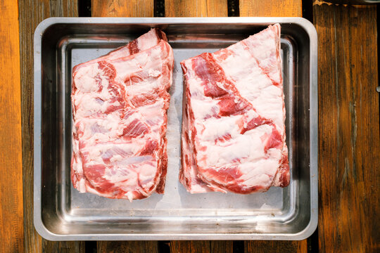 St. Louis Cut Ribs (fleischige Bauchrippen vom Schwein), halbiert in Edelstahlbr&auml;ter auf Holztisch