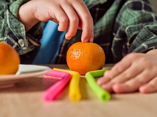 Child making colorful arrangement from drinking straws - A child concentrates as they stick colorful straws into a tangerine, making a playful figure