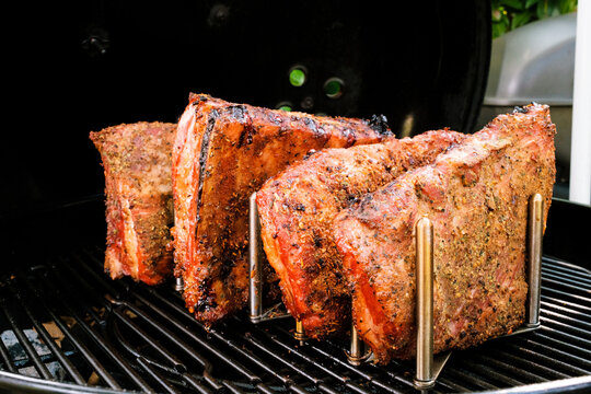 Ger&auml;ucherte St. Louis Cut Ribs (fleischige Bauchrippen vom Schwein) in Rippchenhalter am Grillrost im Kugelgrill