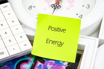 A bright sticky note marked with the words Positive Energy sits beside a calculator and a clock