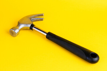 A claw hammer with a black handle on a bright yellow background