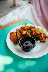 Chicken Wings mit Barbecue Sauce in Schälchen auf Teller am Tisch © Michael