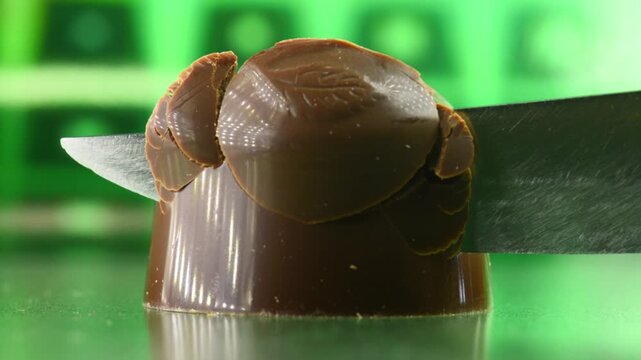Cutting a chocolate candy with a knife, the filling with liqueur and cherry flows out of the candy, close-up.