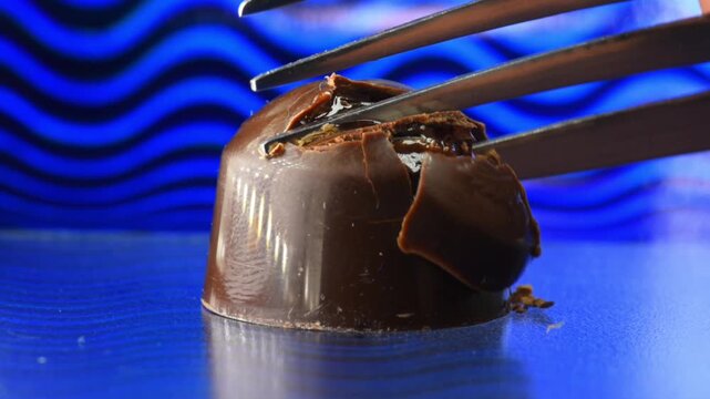 Opening a chocolate candy with a fork, the filling with liqueur and cherry flows out of the candy, close-up.