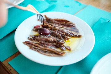 Eingelegte Anchovis (Sardellen) in Öl mit Olive am Tisch, Gabel greift hin