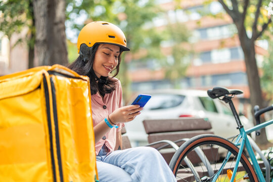 Asian woman delivery rider checking smartphone on break - Powered by Adobe