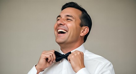 A man in a white shirt and black bow tie laughs heartily while adjusting his tie.