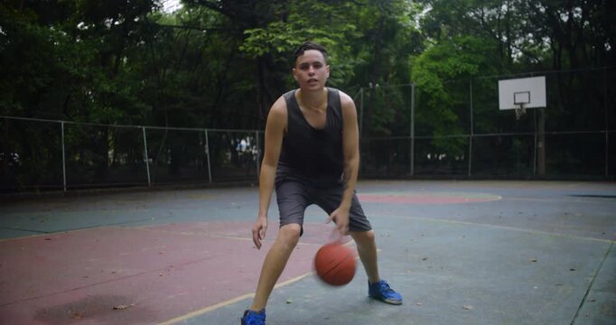 Hispanic man dribbling basketball on outdoor urban court, focused and balanced stance showing coordination, athletic movement, and concentration in relaxed park environment