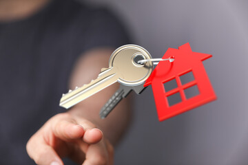 Close up shot of a hand holding house keys with a red house-shaped tag, symbolizing homeownership,...