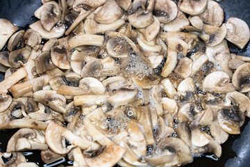 Sliced champignon mushrooms frying in a pan with golden tones